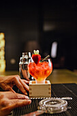 A professional bartender skilfully prepares a lively cocktail in a modern cocktail bar, garnished with a fresh strawberry. The atmosphere is inviting and stylish.