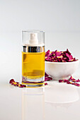 A beautiful glass bottle filled with aromatic rose essential oil stands elegantly next to a bowl of glowing dried rose petals, creating a peaceful and inviting atmosphere.