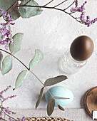 Top view of a delicate Easter table with naturally coloured eggs in soft blue and brown tones, complemented by subtle floral decorations and rustic textures. A cheerful and stylish celebration of spring.