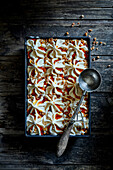 Homemade caramel ice cream with caramel sauce and caramelised walnut pieces in a baking dish on a dark wooden base with an old ice cream scoop