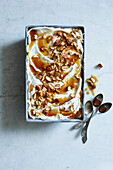 Bowl filled with white homemade ice cream, roasted almonds and maple syrup, top view on a white marble base