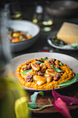 A side view of a plate of gnocchi and sausage with sage on a pumpkin sauce. A bottle of olive oil is in soft focus on the left-hand side of the picture, drawing attention to the plate of gnocchi. In the background, two glasses of white wine in a rustic, autumnal table setting.