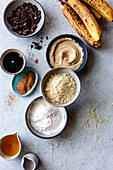 An assortment of baking ingredients, including bananas, chocolate and various powders, arranged on a kitchen table.