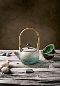 Original handmade ceramic teapot with wooden handle and cups for traditional Chinese tea drinking on an old wooden table. Decorative pebbles all round. Copy space