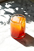 Aperol Spritz on marble surface with shade and hard sunlight, garnished with orange slice