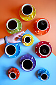 Colourful cups with black coffee. Retro colour block aesthetic. Female hand reaches for an espresso cup.