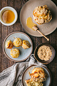 A flat picture of a rustic wooden table with a light grey cloth, honey in a white bowl, a bowl of sesame seeds and sesame muffins on beautiful natural-coloured plates, with a wooden honey spoon. The muffins are all sprinkled with sesame seeds.