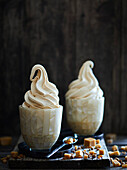 Two sundaes filled with caramel soft serve ice cream, on a dark wooden base