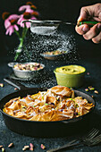 Side view of a cast-iron pan with curled phyllo, action with male hand holding a sieve with icing sugar