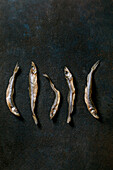 Pile of dried sea fish smelt, ham and anchovies in a row on a dark textured background. Salty traditional starter. Seafood background