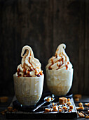 Two sundaes filled with caramel soft ice cream, caramel sauce and toffee pieces on a dark wooden base