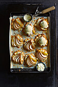 Freshly baked pear and almond cake, on brown baking paper, finished with vanilla ice cream on a black baking tray