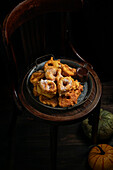Pumpkin donuts, Spanish dessert, Buñuelos de calabaza, la receta tradicional valenciana, wooden chair. The dark background, autumnal theme, large pumpkin under chair