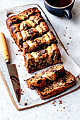 A sliced banana and chocolate chip sandwich lies on a wooden board next to a knife and a cup of coffee.