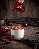 Baked autumn fruit with chopped nuts and maple syrup, with a hand pouring honey over it