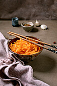 Korean and Asian cuisine dish: vegetable salad with marinated carrots and garlic. Served in a ceramic bowl with chopsticks. Spices in small bowls on the table with mocha mousse notes. Healthy food. Close-up