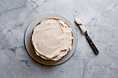 A cake with creamy icing on a marble surface, accompanied by a butter knife.
