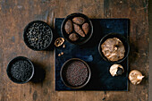 Set of five black spices: black fermented garlic, black Himalayan salt, black mustard seeds, black cardamom and fermented campota pepper in black ceramic bowls. Dark wooden background. Close-up
