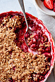 Close-up of a freshly baked strawberry crumble with a spoon showing juicy berries and a golden oat topping.