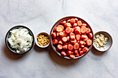 A selection of chopped vegetables, including sliced onions, diced ginger and sliced garlic, together with a large bowl of carrot slices on a light-coloured work surface.