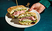 Delicious Italian mortadella sandwich with pesto and mozzarella basil pesto, crusty ciabatta bread, in your hands, in front of a deep green fabric background