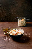 Traditional starter: Sauerkraut with carrots in a bowl and a glass. Sea salt, olive oil and fork nearby. Healthy food, fermented products. Brown textured table.
