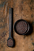 Black mustard seeds for cooking Dijon mustard in a black ceramic bowl with spoon on a dark wooden table. Healthy food, spicy cooking ingredients, traditional cuisine. View from above