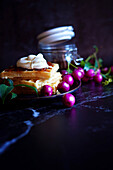 Australian Lilly-Pilly-Riberry jam against a black background, served with waffles and cream. Negative copy space.