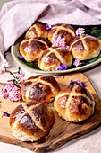 Traditional hot cross buns on a wooden board. Easter baking with spices and dried fruit, decorated with spring flowers. Homemade sweet buns with a cross pattern