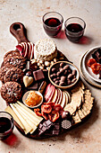 A selection of snacks, including biscuits, cheese, fruit, chocolate and glasses of red wine, beautifully arranged on a wooden board.