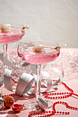 Festlich gedeckter Neujahrstisch, zwei rosafarbene Cocktails garniert mit Litschi und Häppchen, rote Perlen, silberne Bänder, funkelnde Ornamente, für Weihnachtsfeiern