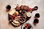 Eine Auswahl an Snacks, darunter Käse, Kekse, Trockenfrüchte und Schokolade, auf einem Holzbrett arrangiert, begleitet von Gläsern mit Rotwein.