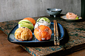 Temari Sushi. Trendy sushi balls with salmon, avocado, cucumber and Japanese omelette on a blue plate. Soya sauce, pickled ginger, chopsticks on a rustic wooden table.