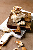 Traditional Spanish dessert, classic crunchy turron with almonds, broken into pieces on a wooden serving board. Beige-coloured, textured background. Top view, distance
