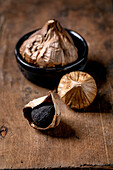 Whole black fermented garlic and peeled garlic clove on a dark wooden table. Healthy nutrition, spicy cooking ingredients, Asian cuisine