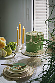Scene of an autumn-winter afternoon with a cake in green. Candles, fruit, flowers and shrubs. Cutlery and plates in gold and green.