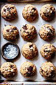 Biscuit dough with oat flakes and chocolate chips and sprinkling salt on a baking tray