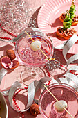 Festlich gedeckter Neujahrstisch, zwei rosa Cocktails garniert mit Litschi und Häppchen, rote Perlen, silberne Bänder, glitzernde Ornamente, für Weihnachtsfeiern