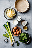 A selection of cooking ingredients such as leeks, spinach, eggs and dairy products on a marble worktop, ready for the preparation of a recipe.