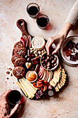 An inviting charcuterie platter with various cheeses, biscuits, fruit, nuts and chocolate, accompanied by a glass of red wine.