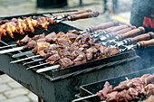 Juicy meat skewers prepared on metal skewers with wooden handles. Grilled chicken and beef pieces on a hot grill with smoke. Preparation of street food in the open air.