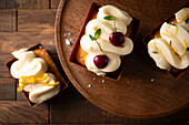 Three mini cakes with icing and fruit garnishes on a wooden backdrop