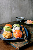 Temari Sushi. Trendy sushi balls with salmon, avocado, cucumber and Japanese omelette on a blue plate. Soya sauce, pickled ginger, chopsticks on a rustic wooden table.