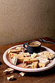 Traditional Spanish dessert, classic soft orange turron and crunchy almond turron, cut into pieces on a rustic clay plate. Espresso in a black cup, wooden table, copy room.