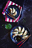 Steamed Japanese vegetable gyoza dumplings with soya, sesame oil and rice vinegar sauce on a black marble background.