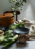 Bowl of soba noodles in spicy broth with baby bok choy, surrounded by fresh mushrooms and ginger