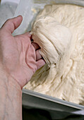 Close-up of a woman kneading raw bread dough in a plastic container. Homemade baking process. Elasticated yeast dough preparation for baking.