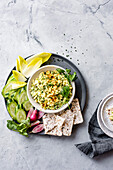 A plate with a bowl of creamy salad, garnished with herbs, surrounded by cucumber slices, endive leaves, radishes and rice cakes.