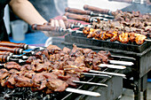 Delicious grilled meat skewers on a hot charcoal grill. Juicy beef and chicken skewers, prepared at a food market or festival.