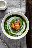 A bowl of spinach cream stands on a wooden table. Golden croutons are carefully arranged on the surface of the cream, creating an attractive contrast of colour and texture. View from above.